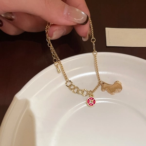 Detail of gold-plated bracelet featuring red coin charm and matte textured dog pendant