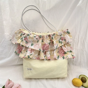 Detail van een crème draagtas met bloemen ruches en een klein merklabel op de tas