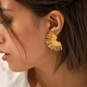 Golden fan-shaped stainless steel stud earrings with sunburst design on model