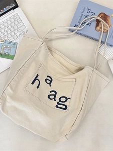 Cream canvas tote bag with haag print shown on desk with laptop and blue books