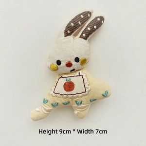 Detail of a 9x7cm handmade fabric bunny doll with carrot embroidery and polka dot ears