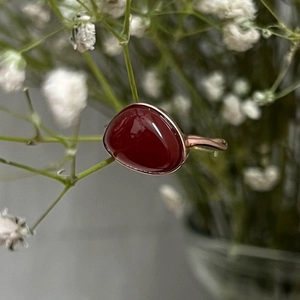 Detail of a rose gold ring with an oval red gemstone set against white flowers