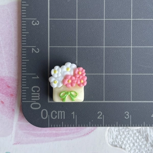 Detailed macro view of a 1.5cm resin flower bouquet charm with a green bow on a scale mat