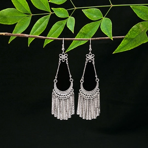 Detailed view of ethnic silver tassel earrings with geometric hollow patterns on a branch