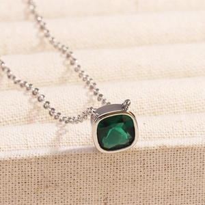 Macro detail of square green emerald pendant with elegant silver chain on beige fabric
