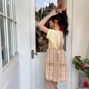 Detail of checkered canvas tote bag with GROCERY text print shown on a model