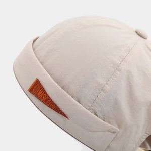 Detailed close-up of quick-dry beige brimless cap featuring a refined orange logo patch