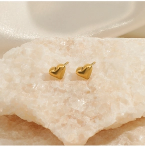 Vue détaillée des boucles d'oreilles cœur dorées sur fond de pierre blanche naturelle
