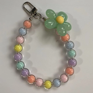 Detail of colorful beaded phone strap featuring a large green flower pendant and metal clasp