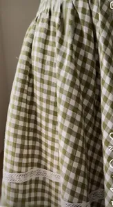 Close-up of green gingham dress featuring delicate white lace trim and ruched hem details