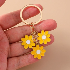 Daisy flower keychain with three yellow charms and gold metal chain on a beige background