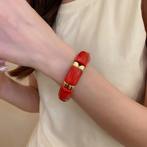Close-up of a red acrylic and gold metal beaded bracelet worn on a woman's wrist