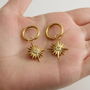Gold starburst hoop earrings with sparkling center crystals held in palm for size