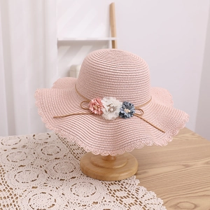 Détail du chapeau de soleil rose en paille avec fleurs décoratives et ruban élégant