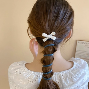 Détail d'un nœud nacré blanc et d'un élastique spirale bleu sur une coiffure tressée
