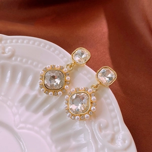 Detailed macro view of vintage square zircon earrings with pearl accents on ceramic plate