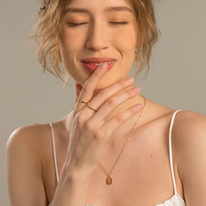 Close-up of a gold rose pendant necklace and layered rings on a fashion model