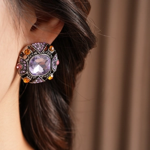 Macro detail of vintage square earrings with purple crystal and intricate filigree work