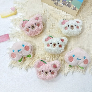 Detailed view of plush strawberry bear and peach brooches on textured cream background