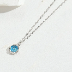 Macro shot of silver chain with a round blue enamel dolphin pendant and zircon borders