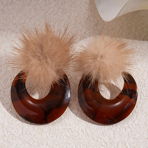 Detail of retro resin earrings with brown tortoiseshell pattern and soft pom-poms