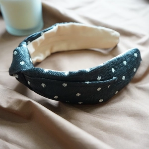 Close-up of black raffia headband with white polka dots on soft brown fabric background