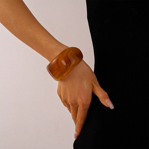 Detail view of a wide amber acrylic bangle with swirly patterns worn by a model