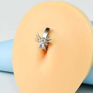 Macro shot of silver spider belly ring with zircon on a realistic silicone navel model