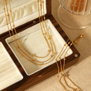 Gold-tone triple-layered bead chain necklace displayed on a beige jewelry box padding
