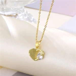 Collier cœur doré avec détails texturés et pierre précieuse sur tissu beige