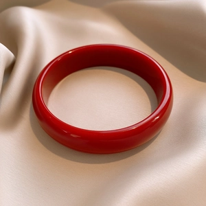 Detailed close-up of glossy red resin round bangle on soft champagne silk fabric