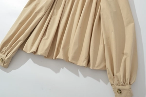 Détail de l'ourlet plissé kaki et des manches bouffantes avec bouton en ambre