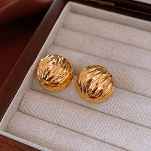 Detail shot of golden spherical stud earrings with faceted metal texture in a jewelry box