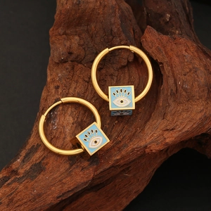 Gold hoop earrings with blue enamel evil eye square pendants on a dark wooden surface