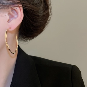 Detailed view of twisted gold-finished hoop earrings worn by a model in a black blazer