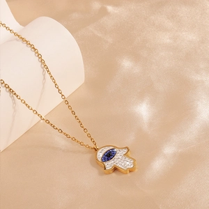 Macro shot of gold Hamsa hand pendant with blue rhinestones on champagne satin