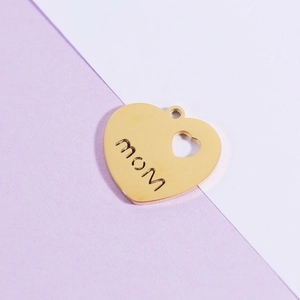 Macro shot of gold heart pendant with MOM engraving and cutout detail on a purple surface