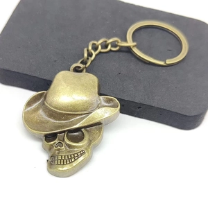 Vintage bronze skull keychain with cowboy hat pendant on grey display cushion