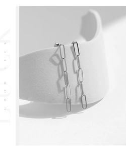 Detail view of silver paperclip chain earrings hanging on a minimalist white prop