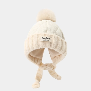 Detail of cream winter knit hat featuring quilted top, soft pom-pom and Bonjour label