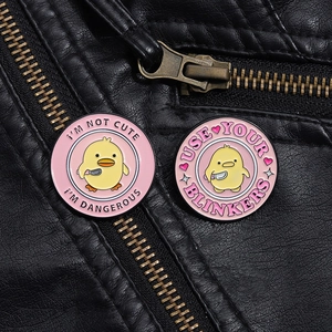 Close-up of yellow duck enamel pins with humorous text on black leather background