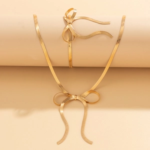Detail view of gold herringbone chain bow necklace and bracelet set on warm beige display