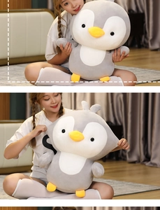 Close-up of a soft grey and white plush penguin pillow with yellow feet and beak