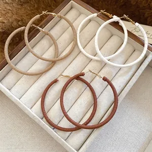 Three pairs of leather-wrapped hoop earrings in beige, white, and brown on a soft white display