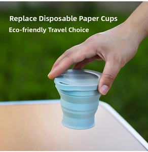 Blue collapsible silicone travel cup held in hand against an outdoor lawn background