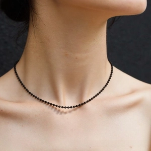 Close-up of minimalist black beaded choker necklace on model against textured background