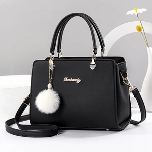 Classic black women's handbag with white fur ball and gold hardware on minimalist background