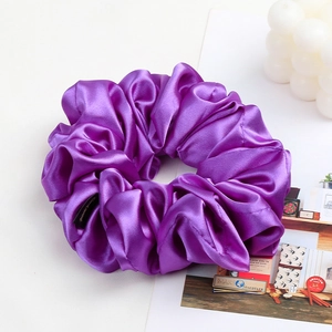 Detail of a large purple satin scrunchie with soft fabric pleats and a black brand label