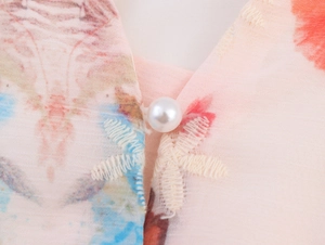 Gros plan sur la broderie florale et bouton perle sur robe en mousseline rose clair