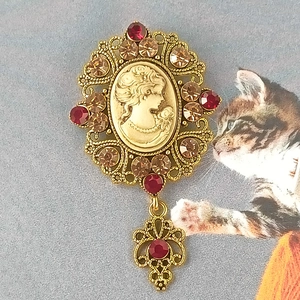 Dettaglio di spilla cammeo vintage con cristalli rossi e silhouette dorata